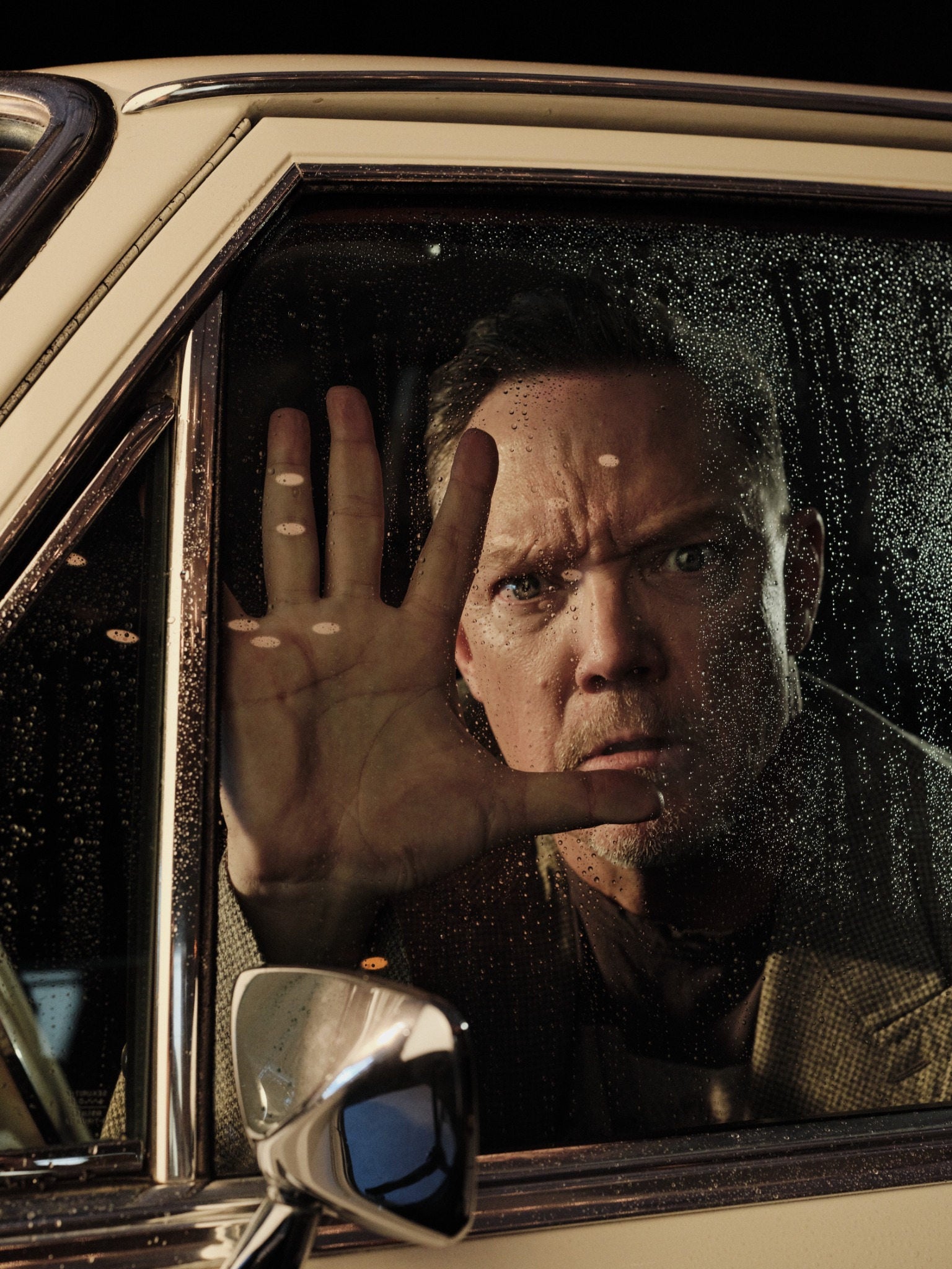 Matthew Lillard seen through the rain-streaked window of a vintage car
