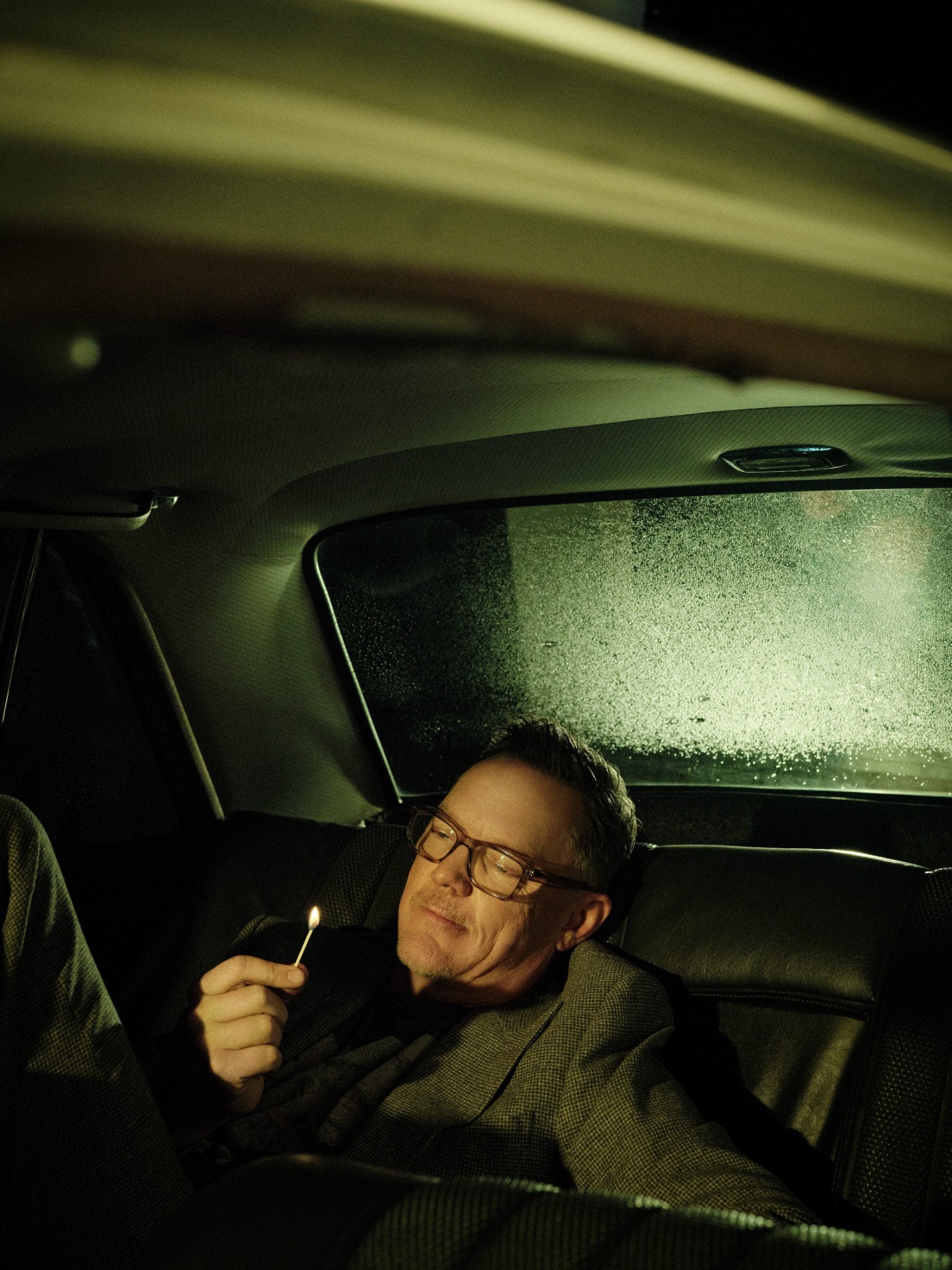 Matthew Lillard holding a match in a green-lit car